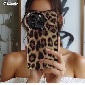 May include: A leopard print phone case with a black camera lens cutout. The case is made of a soft, flexible material and has a sleek, modern design.