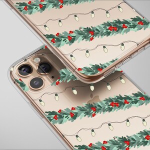 May include: Two clear phone cases with a festive design. The cases feature a repeating pattern of green garland, red berries, and string lights. The cases are made of a clear material, allowing the phone's colour to show through.