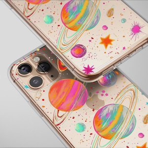 May include: Two clear phone cases with a colorful space-themed design. The cases feature planets with rings, stars, and splashes of pink, orange, and blue. The cases are made of clear plastic and have a gold-colored frame.