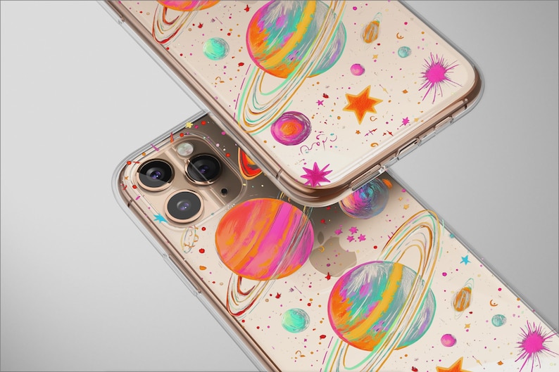 May include: Two clear phone cases with a colorful space-themed design. The cases feature planets with rings, stars, and splashes of pink, orange, and blue. The cases are made of clear plastic and have a gold-colored frame.