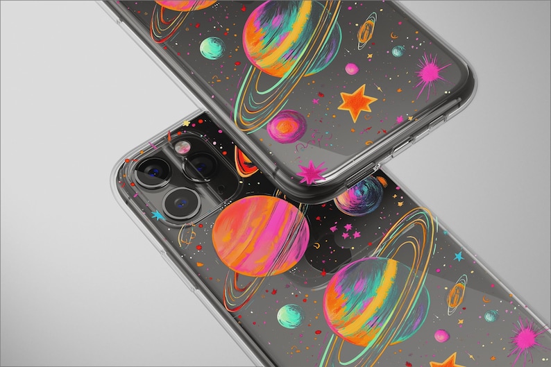 May include: Clear phone cases with a colorful space-themed design. The cases feature planets with rings, stars, and splashes of pink, orange, and blue on a dark background. The cases are shown stacked.