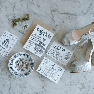 May include: Wedding invitation suite with a save the date card, RSVP card, and invitation card. The cards feature hand-drawn illustrations of a wedding cake, champagne glasses, and a floral arrangement. The text on the cards reads "Save the Date", "RSVP", and "Austin & Trinity".