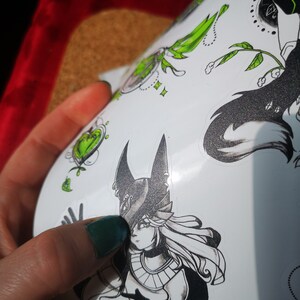 May include: A sheet of stickers featuring black and white illustrations of a woman with a pointed hat, a wolf, and a heart. The stickers have green accents.