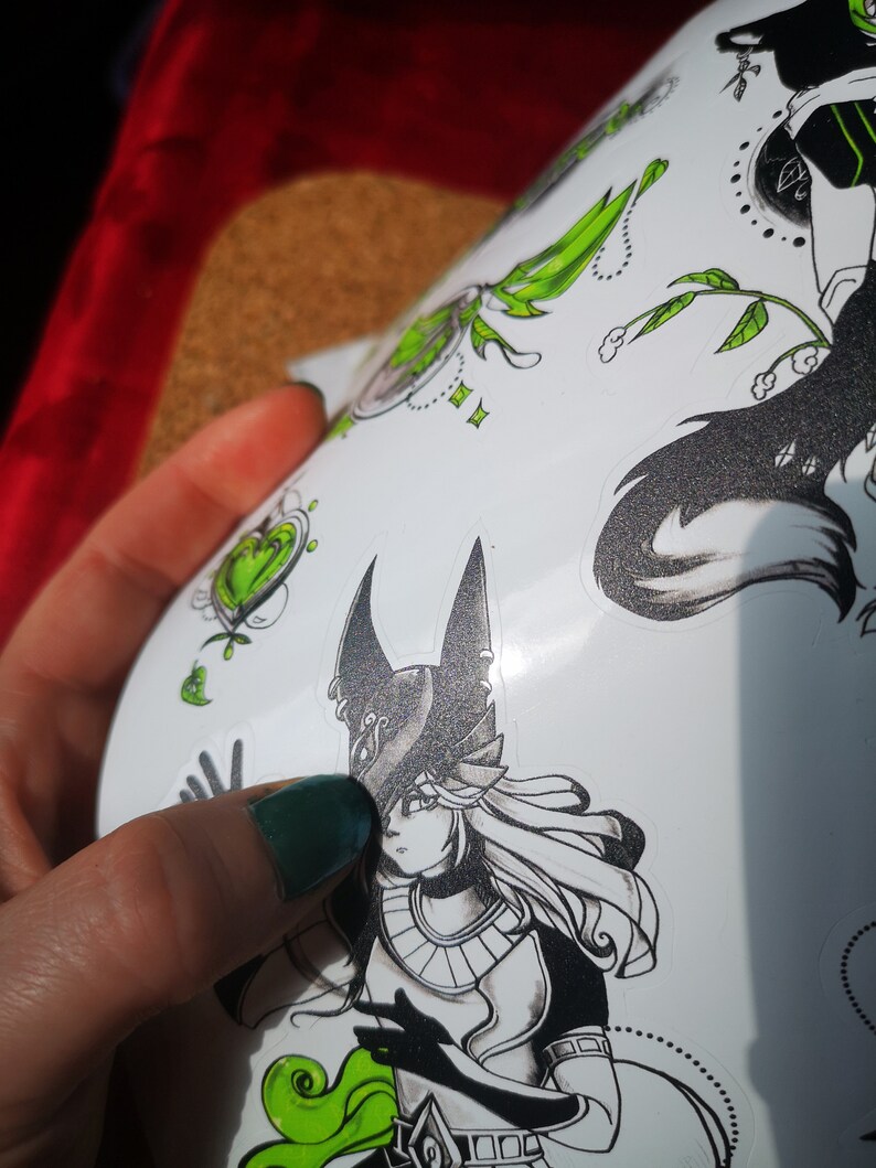 May include: A sheet of stickers featuring black and white illustrations of a woman with a pointed hat, a wolf, and a heart. The stickers have green accents.