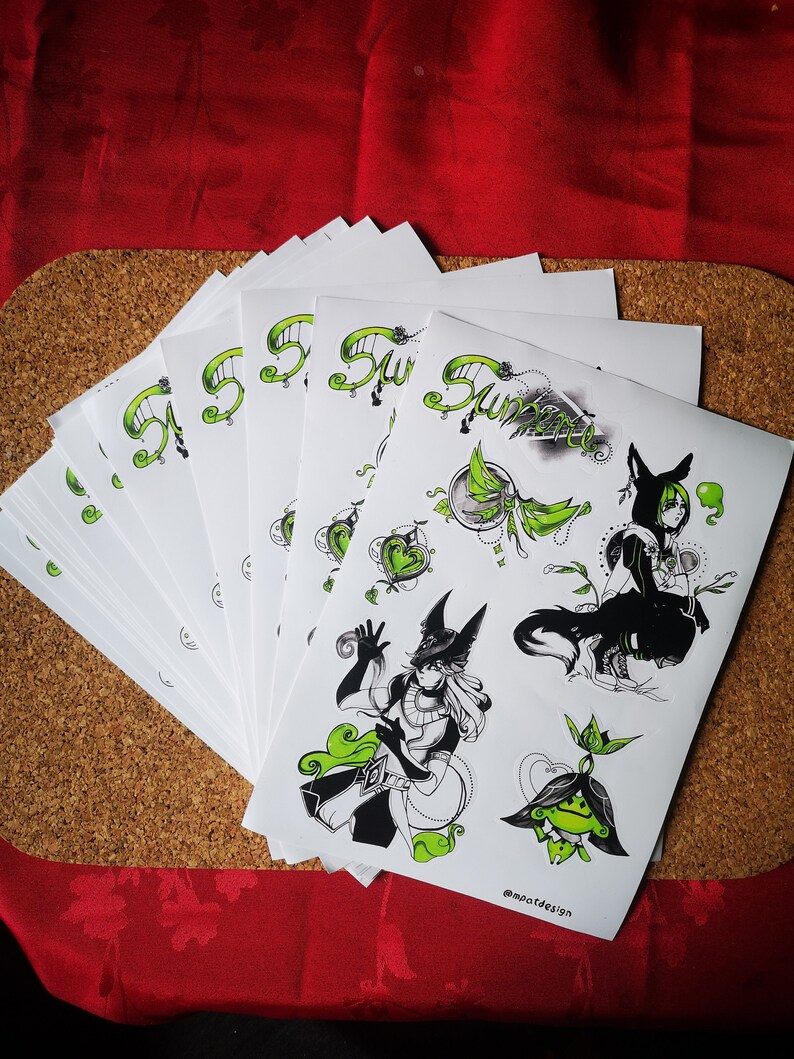 May include: A stack of white stickers with black and green illustrations of a character with a wolf head and a plant. The text "Summer" is written in green on the stickers. The stickers are on a cork surface.