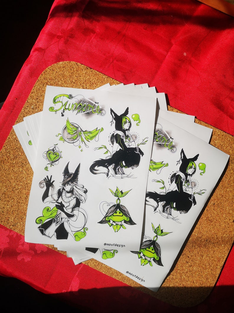 May include: A stack of white stickers with black and green illustrations of a wolf-like creature, a plant, and a person wearing a hooded cloak. The text "@mpatdesign" is printed on the stickers.