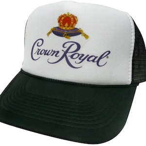 May include: A white and black trucker hat with a purple Crown Royal logo and a gold crown on a purple pillow. The text "Crown Royal" is in a cursive font.