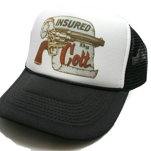 Puede incluir: Gorra de camionero negra y blanca con un panel frontal blanco que presenta una ilustración vintage de un revólver y el texto "INSURED By Colt".