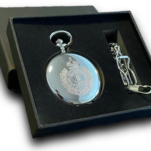 Peut inclure: Une montre de poche argentée avec une chaîne dans un coffret en velours noir. Le cadran de la montre est gravé d'un motif avec une couronne et une lettre P.
