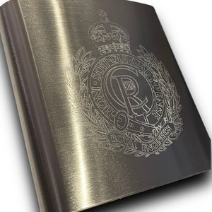 May include: A stainless steel flask with a brushed metal finish. The flask features an engraved emblem with the words "Royal Engineers" and a crown. The flask has a silver cap.
