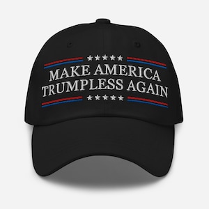 Op de afbeelding: Zwarte baseballcap met de geborduurde tekst "MAKE AMERICA TRUMPLESS AGAIN" in het wit. De tekst is omlijst door rode en blauwe strepen en sterren.