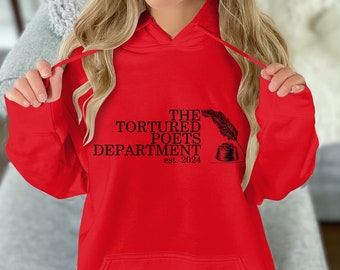 May include: Red hooded sweatshirt with the text "The Tortured Poets Department est. 2024" and a black and white illustration of a quill pen and inkwell.
