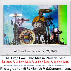 May include: A live concert photo featuring a drummer playing a drum kit. The bass drum displays the band name "All Time Low" with a skull and crossbones logo and "Baltimore, MD." The drummer wears a yellow shirt and a cap. The photo includes the text "All Time Low - The Met in Philadelphia."