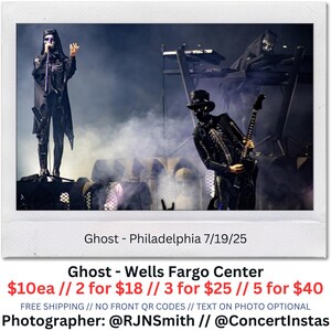 May include: Polaroid-style photo of the band Ghost performing live on stage. The band members are dressed in black costumes with skeleton-like designs. The text "Ghost - Philadelphia 7/19/25" is visible. The photo is taken at the Wells Fargo Center.