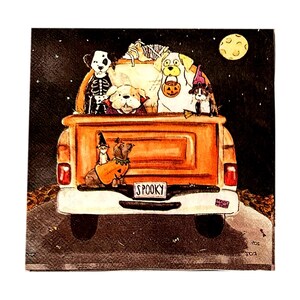 May include: A square decorative napkin featuring an illustration of an orange pickup truck at night under a full moon. The truck bed is filled with dogs in Halloween costumes, including a skeleton, a vampire, and a witch. The license plate reads SPOOKY.