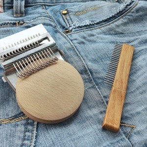 Pode incluir: Um tear de tricô prateado com uma base circular de madeira e um pente de madeira com dentes de metal, ambos sobre um fundo de jeans azul.