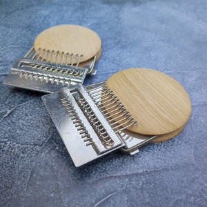 May include: Two silver metal embroidery hoops with wooden rings. The hoops are stacked on top of each other. The top hoop is slightly tilted to the side.