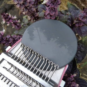 May include: A close-up of a circular grey knitting needle with a metal needle bed attached to the bottom. The needle bed has a series of metal loops that are used to hold the yarn.
