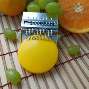 May include: A yellow musical instrument with a metal frame and a row of metal tines. The instrument is sitting on a bamboo mat with green grapes and a sliced orange.