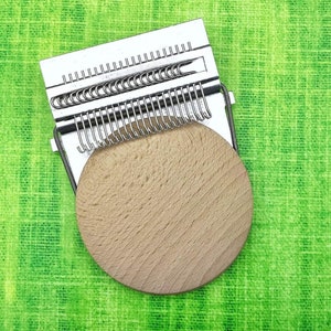 May include: A silver metal yarn winder with a wooden base. The winder has a series of metal hooks that hold the yarn in place as it is wound.
