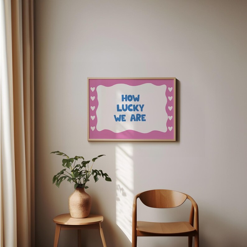 May include: A pink and white framed print with a wavy border and a blue text overlay that reads "How Lucky We Are". The print is surrounded by small white hearts.