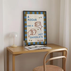 May include: A brown framed poster with a blue and brown striped background. The poster says "A Mocha and a Hot Chocolate Please" with illustrations of two hands holding mugs.