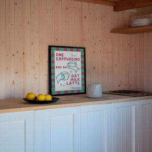 May include: A framed print with a green and pink striped background. The print says "One Cappuccino and an Oat Milk Latte Please".