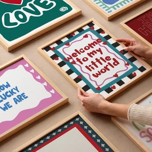 May include: A collection of eight framed prints with various designs and colors. The prints feature text such as "Welcome to my little world", "How lucky we are", and "We are so lucky for days".