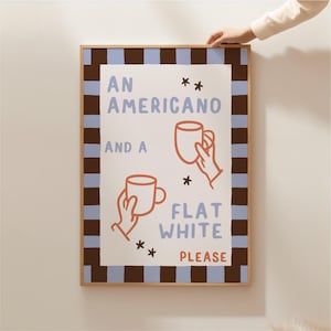 May include: A white framed print with a brown and blue striped border. The print features a hand-drawn illustration of two coffee cups with the text "An Americano and a Flat White Please".