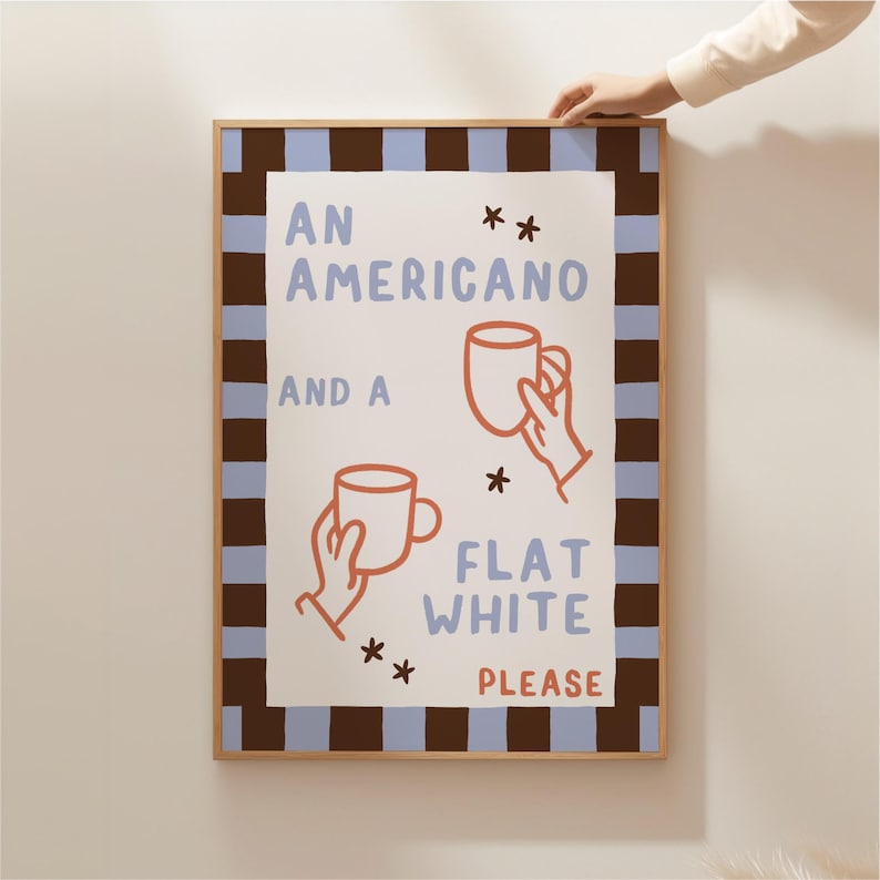 May include: A white framed print with a brown and blue striped border. The print features a hand-drawn illustration of two coffee cups with the text "An Americano and a Flat White Please".