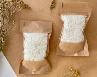 Può includere: Due sacchetti di fiocchi di cera bianca per la fabbricazione di candele. I sacchetti sono in carta marrone e hanno un'etichetta bianca con testo nero. I sacchetti sono su una superficie marrone con fiori secchi.