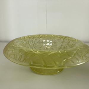 May include: A translucent, pale yellow glass bowl featuring a wide, flat rim decorated with a raised, interconnected geometric lattice pattern. The bowl has a circular base and a shallow, open center, showcasing a smooth, glossy finish throughout.