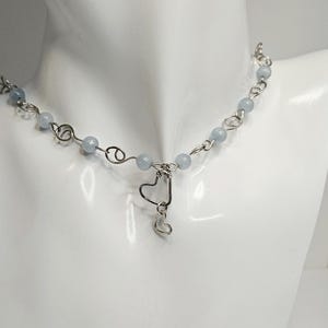 Peut inclure: Un collier en argent avec des perles bleu clair et un pendentif en forme de cœur.
