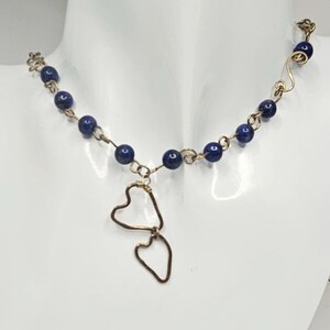 May include: A gold necklace with a pendant of two intertwined hearts. The necklace is made with small, dark blue beads.