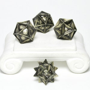 May include: Four antique gold metal dice with a star-shaped design. The dice are sitting on a white pedestal with a scroll design.