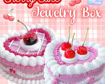 Puede incluir: Dos cajas de joyería en forma de corazón de pastel de cereza rosa con glaseado blanco y cerezas rojas en la parte superior. Las cajas están sobre un fondo a cuadros rosa y blanco. El texto "Cherry Cake Jewelry Box" está en la parte superior de la imagen.