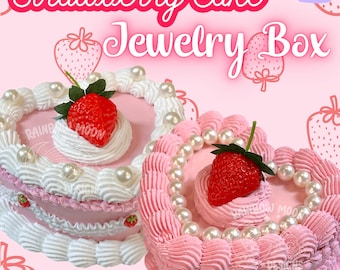 Puede incluir: Dos cajas de joyería en forma de corazón de pastel de fresa rosa y blanco con acentos de perlas. Las cajas están decoradas con glaseado blanco y fondant rosa y blanco.