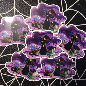 May include: Five black cat witch stickers with a purple, starry background. Each sticker features a black cat wearing a witch hat, a crystal ball, and a stack of books.