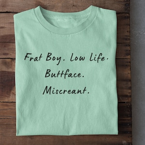 Puede incluir: Una camiseta verde claro con el texto "Frat Boy. Low life. Buttface. Miscreant." impreso en negro.