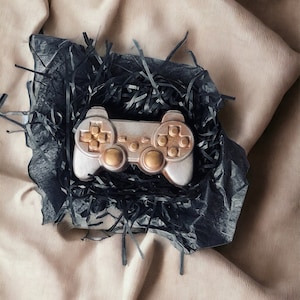 Può includere: Un controller da gioco in cioccolato color oro in una scatola regalo nera con carta da regalo nera.