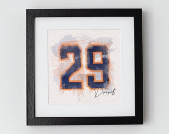 May include: A framed watercolor painting of the number 29 in navy blue with an orange outline. The number is on a white background with orange and blue watercolor splatters. The signature "Leon Draisaitl" is written in black below the number.
