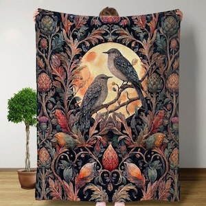 May include: A large, rectangular throw blanket featuring a detailed illustration of two birds perched on a branch in front of a full moon. The blanket has a dark background with floral and botanical elements in shades of orange, green, and brown.