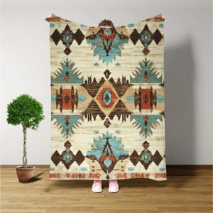 May include: A cream-colored throw blanket with a geometric pattern in shades of brown, blue, and red. The pattern features a central diamond shape with smaller diamonds and triangles surrounding it.