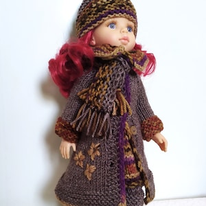 May include: A doll wearing a brown knitted coat with a purple and brown scarf, a brown knitted hat with a purple and brown pattern, and brown knitted boots.