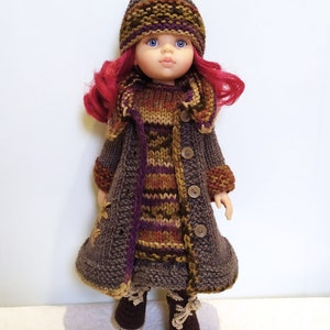 May include: A doll wearing a brown knitted coat with a striped pattern, a matching hat, and brown boots. The doll has pink hair and blue eyes.