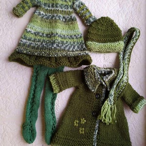 May include: A set of knitted clothing for a doll, including a green and white striped dress, a green coat with a button closure, a green hat, and green tights.