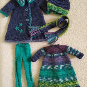 May include: A set of knitted doll clothes in shades of blue, green, and purple. The set includes a coat, dress, leggings, hat, and scarf.