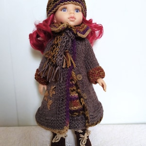 May include: A doll wearing a brown knitted coat with a colorful scarf, a brown knitted hat with purple and green stripes, and brown knitted shoes.