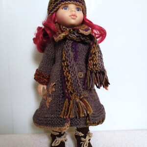 May include: A doll wearing a brown knitted coat with a purple and brown scarf, a brown knitted hat with purple and brown stripes, and brown knitted boots with tan laces.