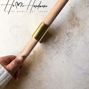 May include: A cylindrical wooden rod featuring a smooth, polished brass connector sleeve at the center. The text Ho Mi Hardware WHERE HOMES ARE LOVED is visible in the upper left corner of the image, presented in a black script and sans-serif font.